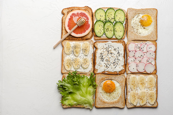 Different toasts on a white background. Toast with egg, banana, salad, cream cheese, cucumber, radish, grapefruit and honey. - Φωτογραφία, εικόνα