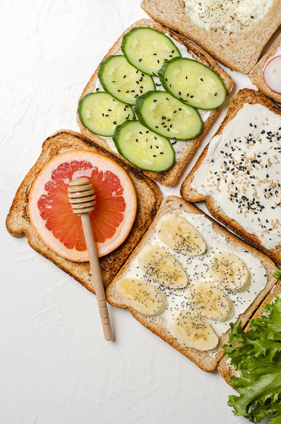 Different toasts on a white background. Toast with egg, banana, salad, cream cheese, cucumber, radish, grapefruit and honey. - Foto, immagini