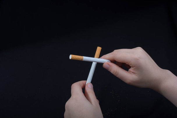 Hand is holding crossed cigarettes on black background - Foto, imagen