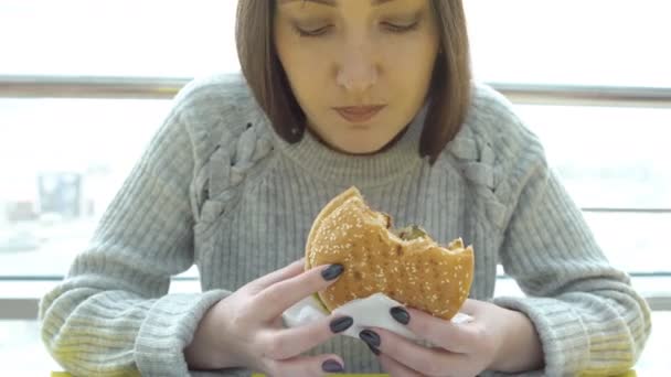 Comida rápida. Mujer joven con apetito comiendo una hamburguesa
 - Imágenes, Vídeo