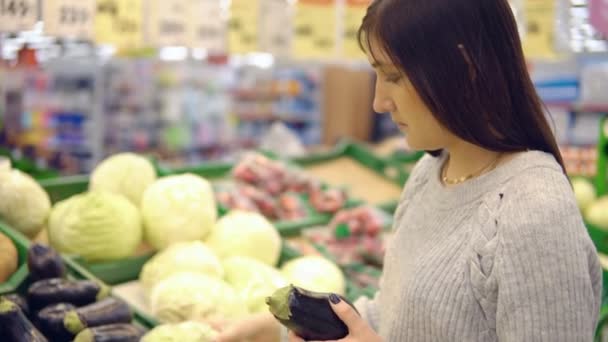 Young woman in the vegetable department of a supermarket chooses eggplant - Video