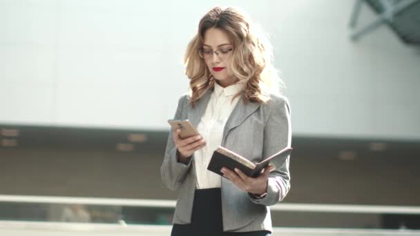 νεαρή γυναίκα στο επαγγελματικό κοστούμι πληκτρολόγηση μηνυμάτων στο κινητό τηλέφωνο. πορτρέτο μιας γυναίκας επιχειρήσεων σε ένα κτίριο γραφείων - Πλάνα, βίντεο