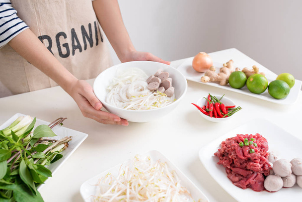 Γυναικεία χέρια μαγειρέματος βιετναμέζικες παραδοσιακή σούπα Pho bo με βότανα, λαχανικά, κρέας, noodles ρυζιού - Φωτογραφία, εικόνα