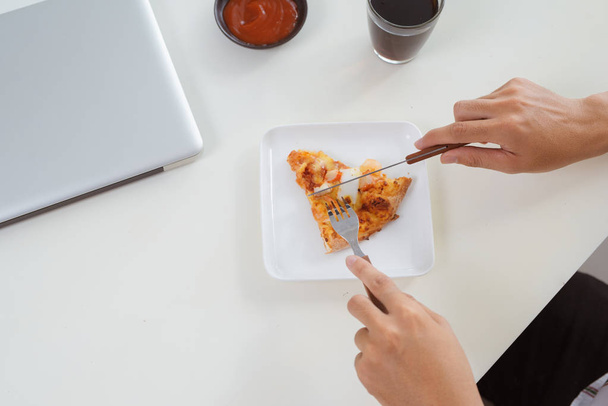 Közelkép a férfi kezében laptop számítógépen dolgozik pizzát eszik - Fotó, kép