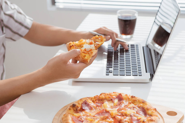 ラップトップ コンピューターで作業してピザを食べる男性の手を閉じる - 写真・画像