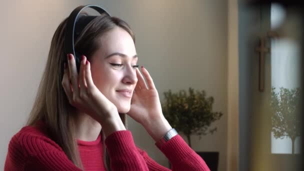 Beautiful Girl Listens to Music in Cafe. Girl in headphones listening to music in a cafe - Filmagem, Vídeo