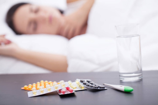 Mujer insalubre dormida y pastillas en la mesita de noche
 - Foto, imagen