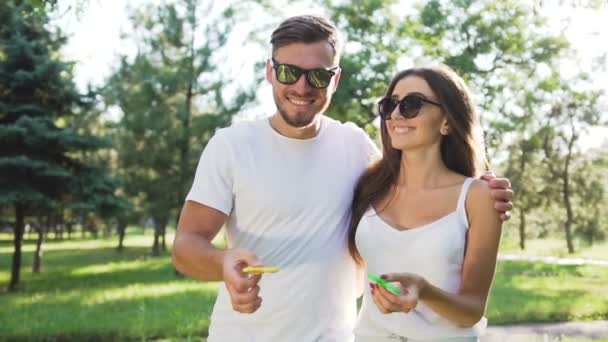 Young couple having fun with a hand spinner in the park. Summer lifestyle concept - Video, Çekim