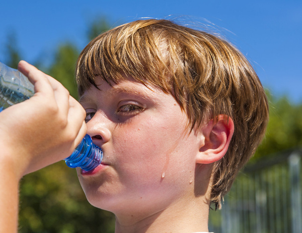 Молодий хлопчик п'є воду з пляшки
 - Фото, зображення