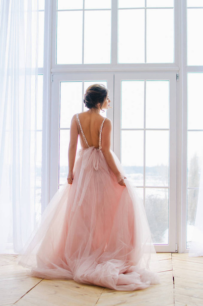 Belle fille dans une robe rose luxueuse est debout près de la fenêtre
 - Photo, image