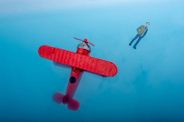 Hand met een modelvliegtuig en een beeldje van de man in blauw water - Foto, afbeelding