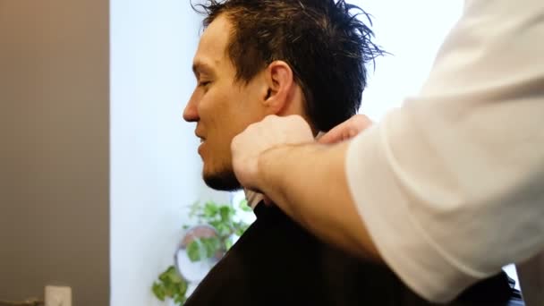 Парикмахер надевает защитный плащ фартука мужчине в салоне красоты
 - Кадры, видео