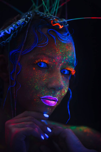 Ritratto al neon di una ragazza. Luminosi spruzzi sul viso. Modello con lenti al neon blu al buio. L'immagine per Halloween
. - Foto, immagini