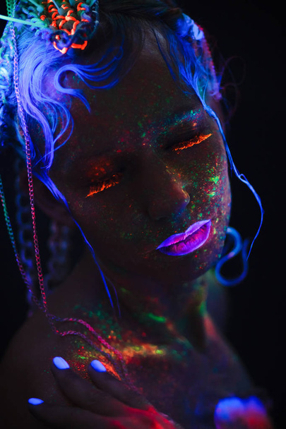 Ritratto al neon di una ragazza. Luminosi spruzzi sul viso. Modello con lenti al neon blu al buio. L'immagine per Halloween
. - Foto, immagini
