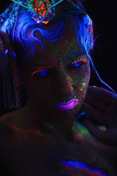 Neon portret van een meisje. Bright spatten op het gezicht. Model met blauwe neon lenzen in het donker. Het beeld voor halloween. - Foto, afbeelding