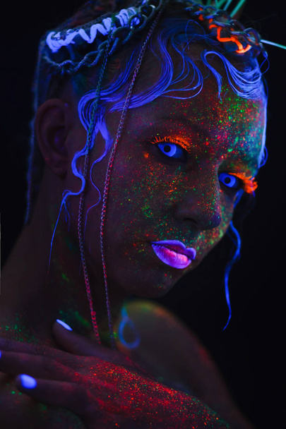 Neon-Porträt eines Mädchens. Helle Spritzer im Gesicht. Modell mit blauen Neon-Linsen in der Dunkelheit. das Bild für Halloween. - Foto, Bild