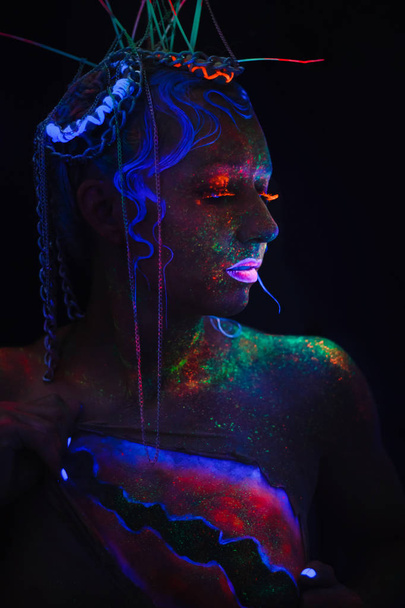 Retrato de néon de uma rapariga. Brilhantes salpicos na cara. Modelo com lentes de néon azul no escuro. A imagem de halloween
. - Foto, Imagem