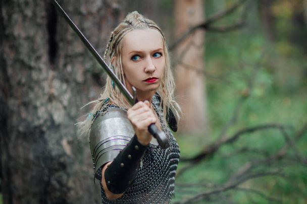 Una hermosa guerrera con una espada y una armadura. Una modelo con una falda de cadena y un chaleco en un bosque misterioso. Foto de fantasía
. - Foto, imagen