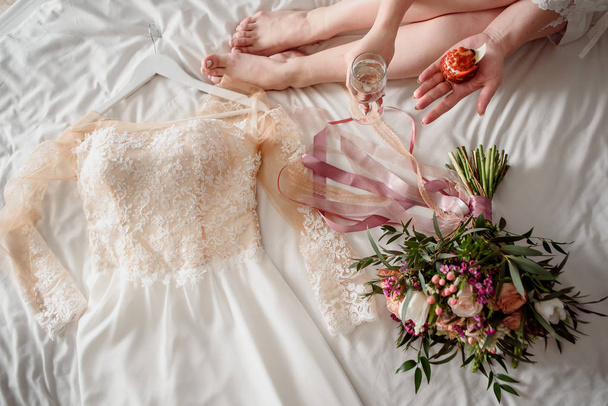 A beautiful wedding dress lies on the bed next to the brides bouquet - Photo, Image