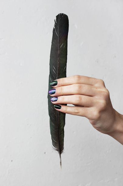 hand of a young girl with green manicure, which shows a sign of biological danger biohazard and black magpie feather. vertical - Valokuva, kuva