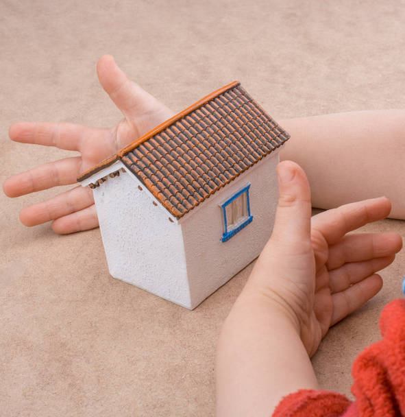 Küçük model ev ve açık kahverengi arka planda bir el. - Fotoğraf, Görsel