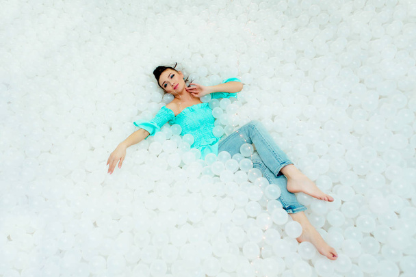 Gelukkig mooie vrouw legt omringd door witte plastic ballen in het droge zwembad voor volwassene. Kopiëren van ruimte. - Foto, afbeelding