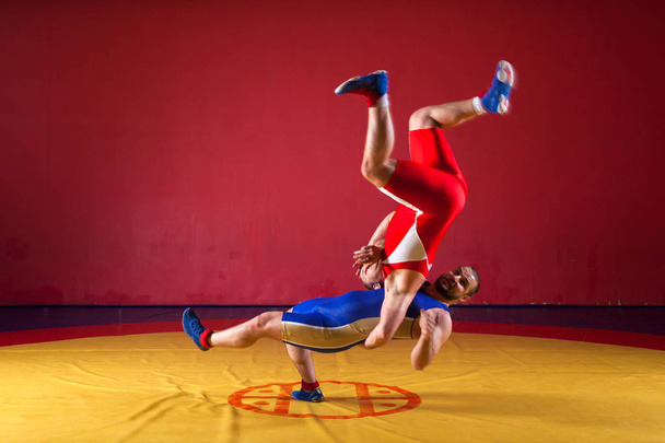 Zwei junge Männer in blauen und roten Wrestling-Strumpfhosen ringen auf einem gelben Wrestling-Teppich in der Turnhalle - Foto, Bild