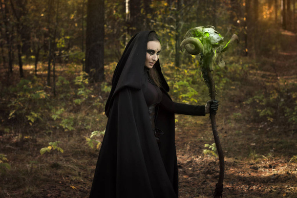 Contos para o Dia das Bruxas, a menina com um pau de caveira de carneiro em um manto preto com um Grimm terrível, uma imagem escura
 - Foto, Imagem