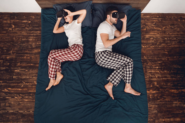 Top view. Young woman and man lie on the bed and look in virtual reality glasses. Home leisure. - Фото, зображення