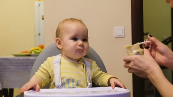 Kislány eszik burgonyapürével a jar egy gyermek széken ül, anya ad otthon a íztelen bébiétel - Felvétel, videó