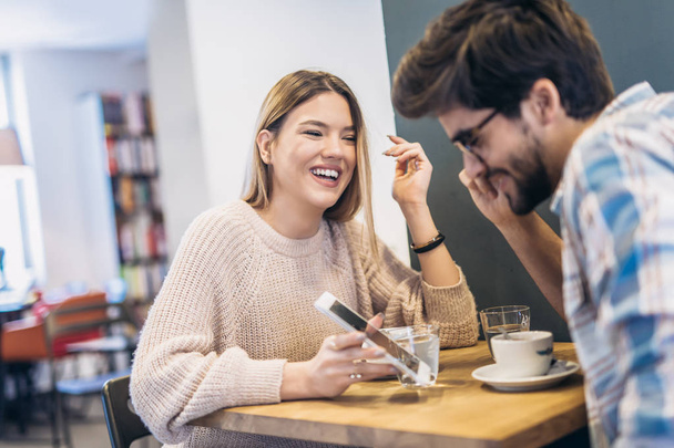 Preciosa pareja con teléfono inteligente y divertirse en la mesa en la cafetería
 - Foto, Imagen