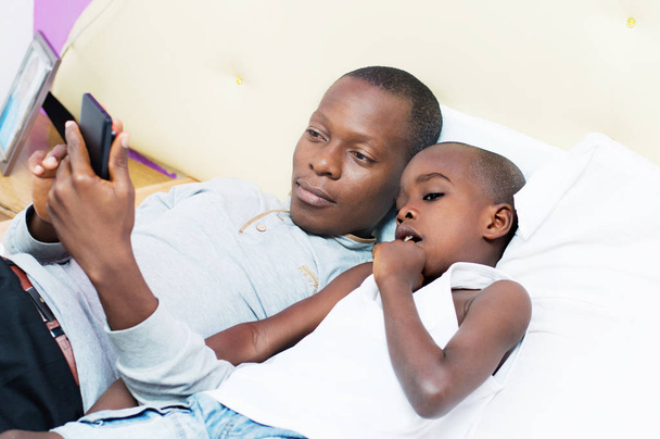 vader en zoon raadpleegt een mobiele telefoon in bed - Foto, afbeelding