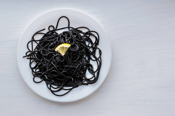 black pasta with slices of lemon in a white plate on a white background - 写真・画像