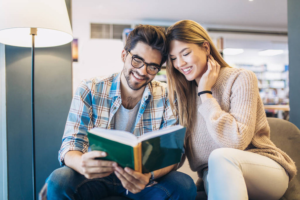 Atractiva pareja joven leyendo libro juntos en la biblioteca
  - Foto, imagen