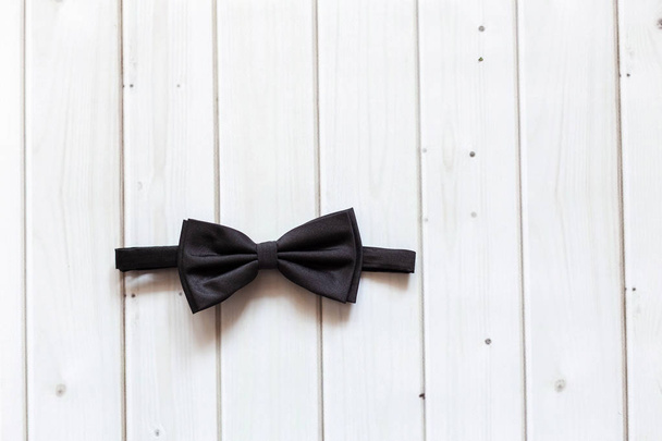 Black bow tie lies on a light wooden background. Closeup - Φωτογραφία, εικόνα