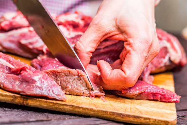 Las manos femeninas cortan carne cruda cerca
 - Foto, imagen