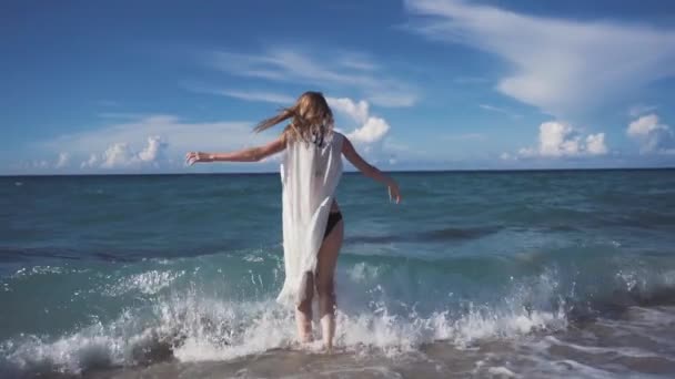Girl, beach, sea, wind in your hair. Beautiful girl smiles and splashes in the waves of the Pacific Ocean. A linen tunic develops in the wind. - Footage, Video