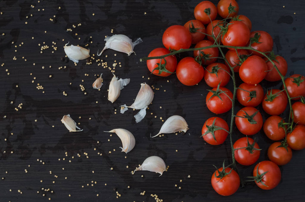 Branch of  tomatoes and garlic on side, on black background with spilled spices - Foto, afbeelding