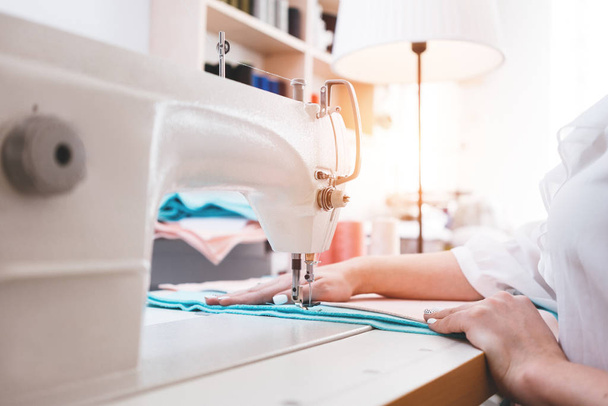 Dressmaker in sew studio working on sewing machine. Woman seamstress making small business - 写真・画像