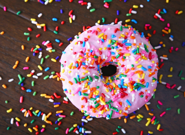 overhead studio shot of a donut with sprinkles on a wooden background unhealthy food concept  - Photo, image