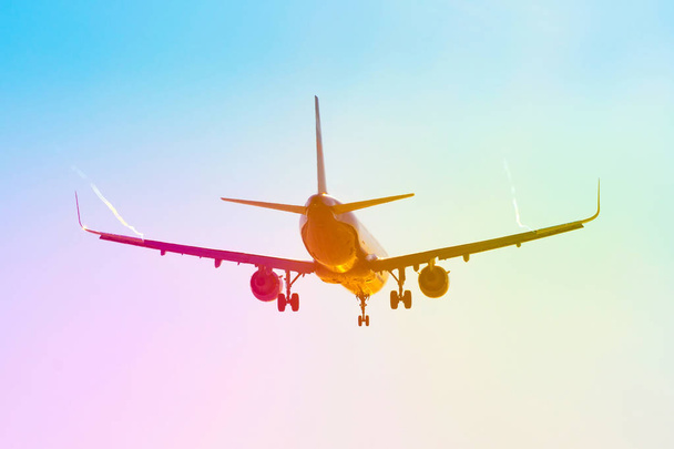 Avión de pasajeros vuela cerca del resplandor del sol con un gradiente de arco iris de color en el aterrizaje, con las alas de un vórtice de chorro de vapor
. - Foto, Imagen