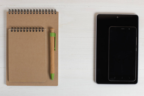 Stylo d'un smartphone en bois naturel et bloc-notes sur une table blanche
. - Photo, image