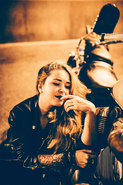 hermosa linda mujer en chaqueta de cuero sentado en el suelo cerca de la moto
  - Foto, Imagen