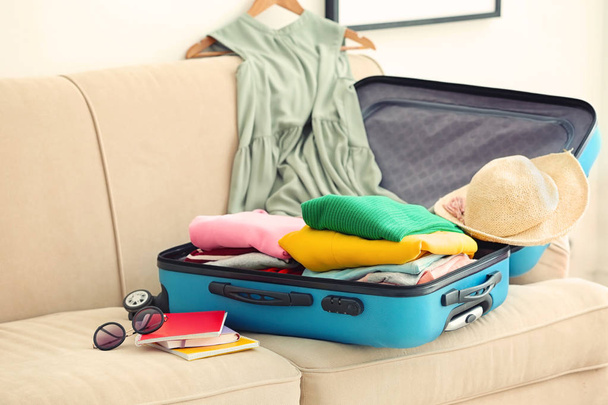 Travel suitcase with clothes and notebooks on sofa - Valokuva, kuva