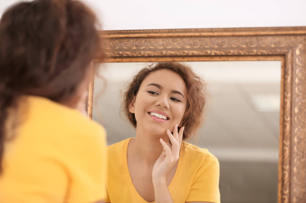 Beautiful young woman with acne problem looking in mirror at home - Photo, image