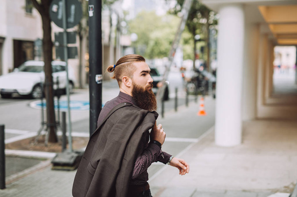 Der junge Mann mit dem Bart geht auf die Straße. auf der Rückseite finden Sie stilvolle klassische Jacke - Foto, Bild