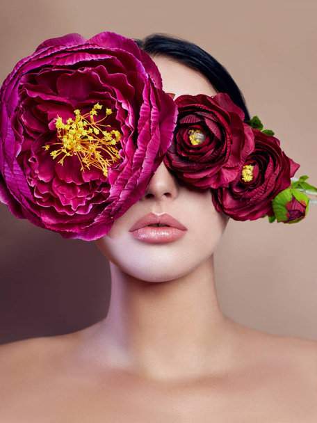 Large peonies near a woman face, art fashion flowers in front of a girl, nature face care, natural cosmetics and professional makeup, beige background. Purity hair eyes and makeup sexy girls. - 写真・画像