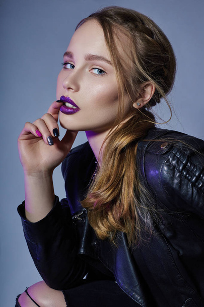 Fashion Vogue girl makeup purple lipstick, woman in leather jacket and black jeans on dark blue background. Daring bright makeup girl is highlighted with purple color. - Foto, Imagen