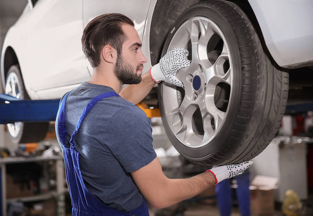 Young mechanic changing wheel at tire service - Фото, зображення
