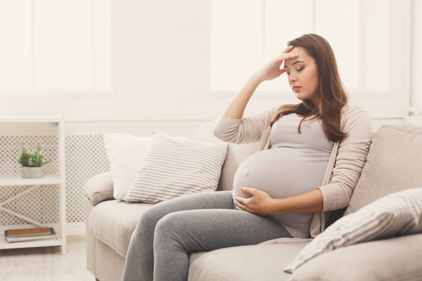 Young pregnant woman with headache sitting on sofa - Foto, imagen